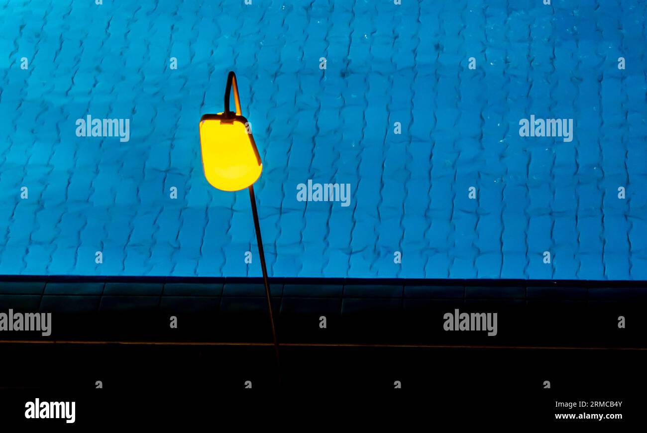 Gelbe Lampe über dem blauen Wasser des Pools, Nachtaufnahme. Stockfoto