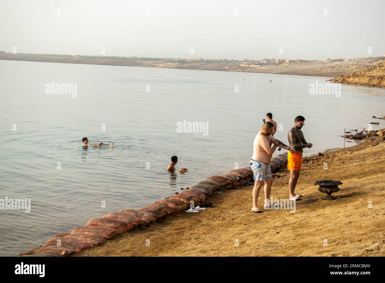 Menschen, die Schlamm aufbringen, bevor sie zum Wasser des Toten Meeres in Jordanien gehen Touristen, die mit Schlamm bedeckt sind, schwimmen im Toten Meer, Jordanien Stockfoto