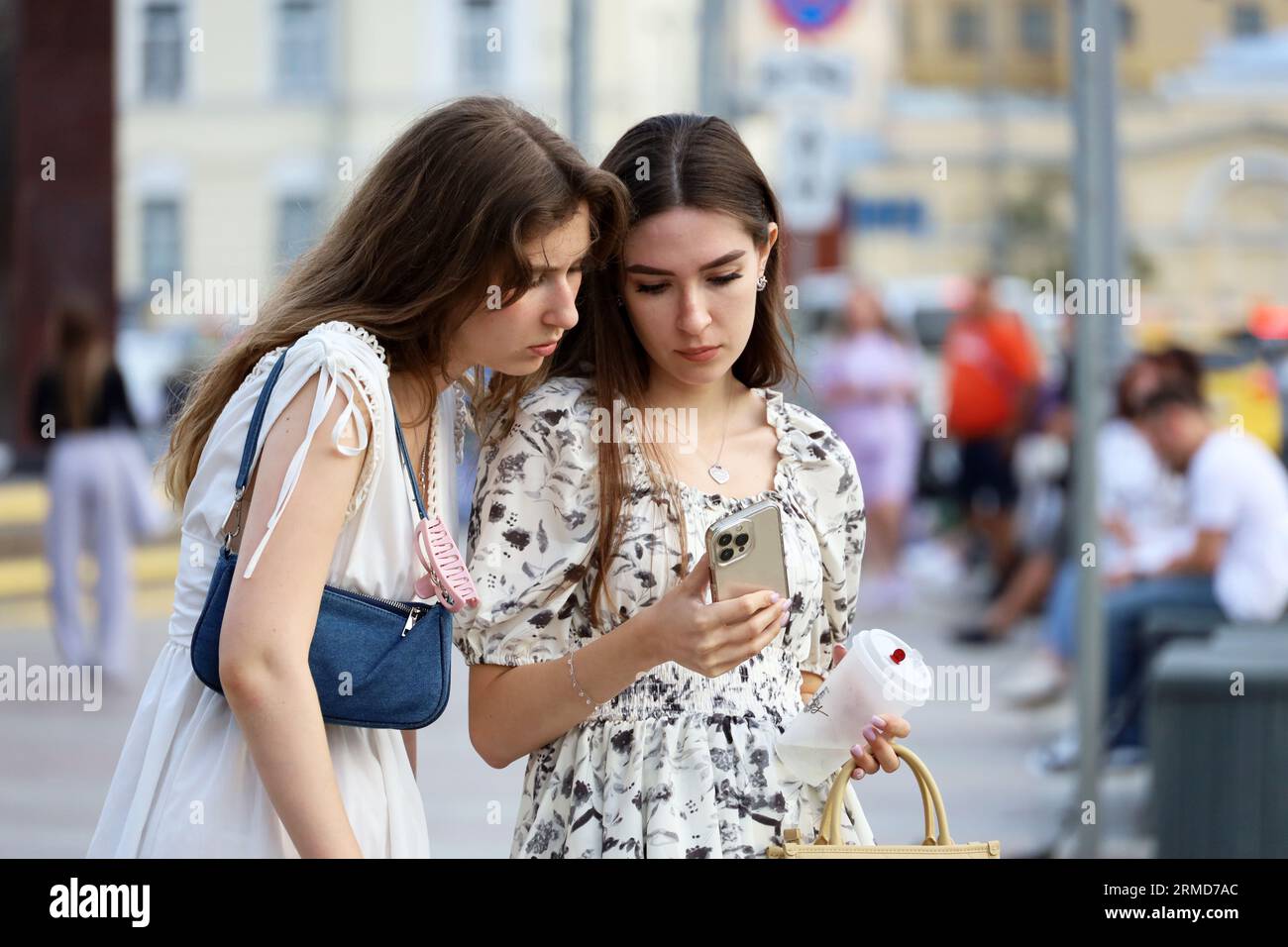 Zwei Mädchen, die im Sommer auf der Straße stehen und auf den Bildschirm des Smartphones schauen Stockfoto