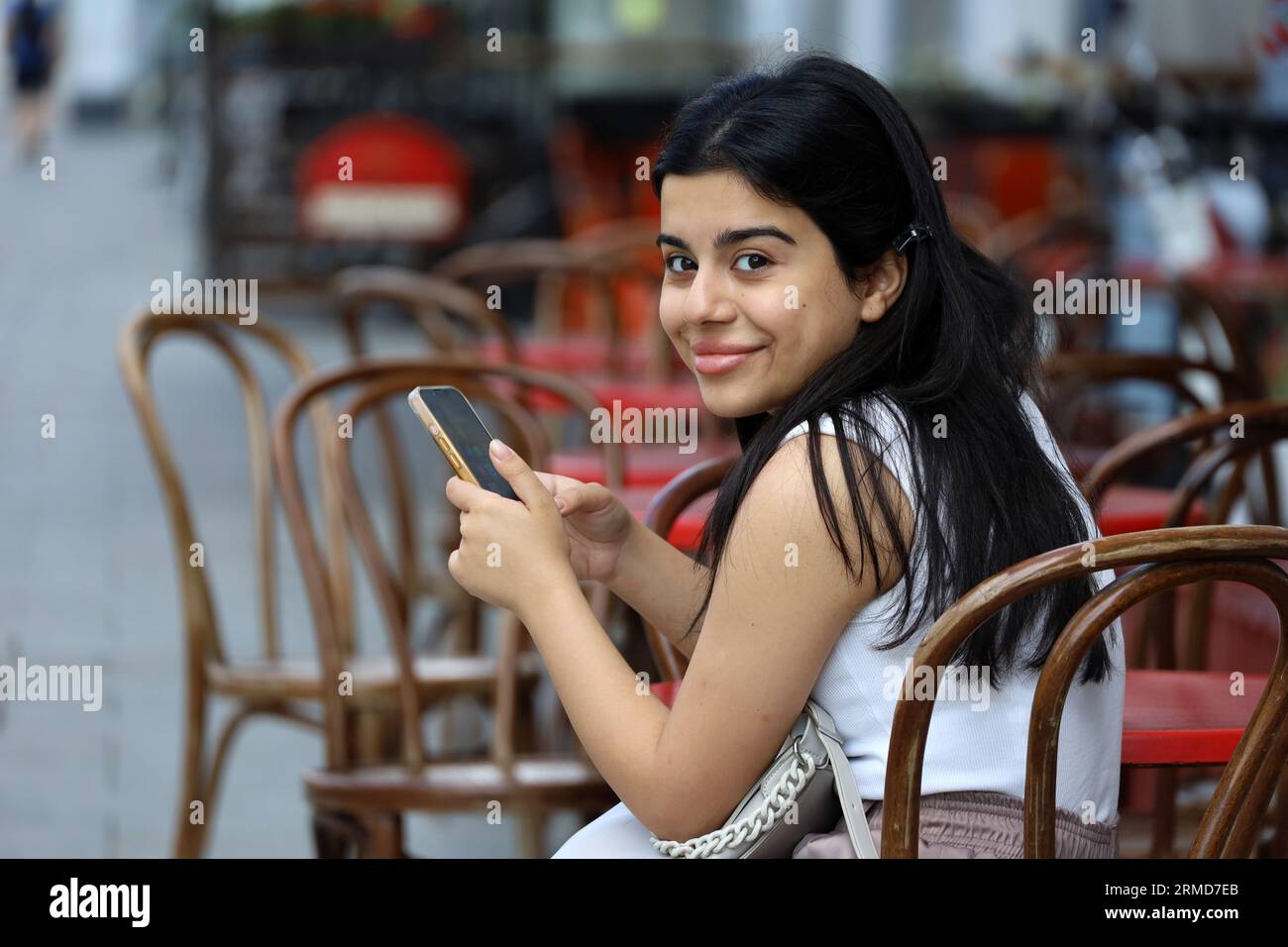 Lächelndes Mädchen, das mit Smartphone im Straßencafé sitzt. Leben in der Sommerstadt, Online-Kommunikation Stockfoto