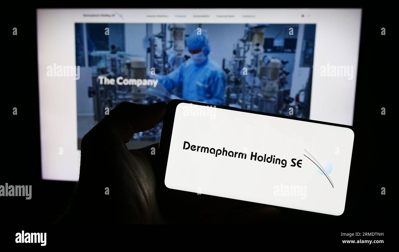 Person, die ein Mobiltelefon mit dem Logo des deutschen Pharmaunternehmens Dermapharm AG auf dem Bildschirm vor der Business-Webseite hält. Konzentrieren Sie sich auf das Display des Telefons. Stockfoto
