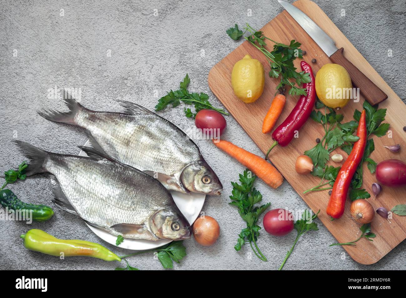 Auf dem Teller sind zwei große Brassen. In der Nähe gibt es Gemüse und Gewürze zum Kochen dieser Flussfisch. Draufsicht mit Kopierbereich. Flach liegend Stockfoto