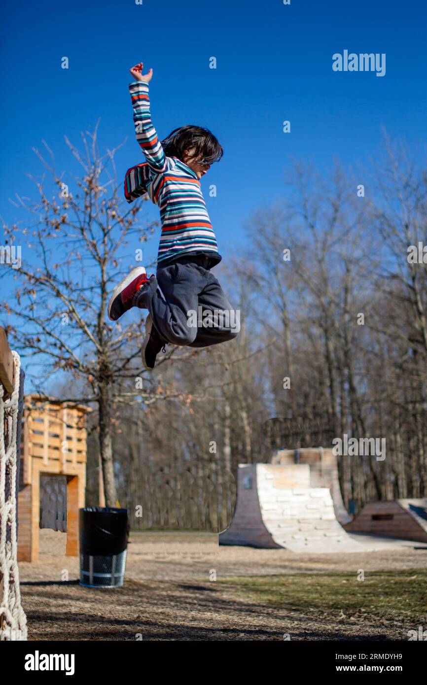 Ein Junge mit den Armen in der Luft springt von einer hölzernen Plattform in einem Park Stockfoto