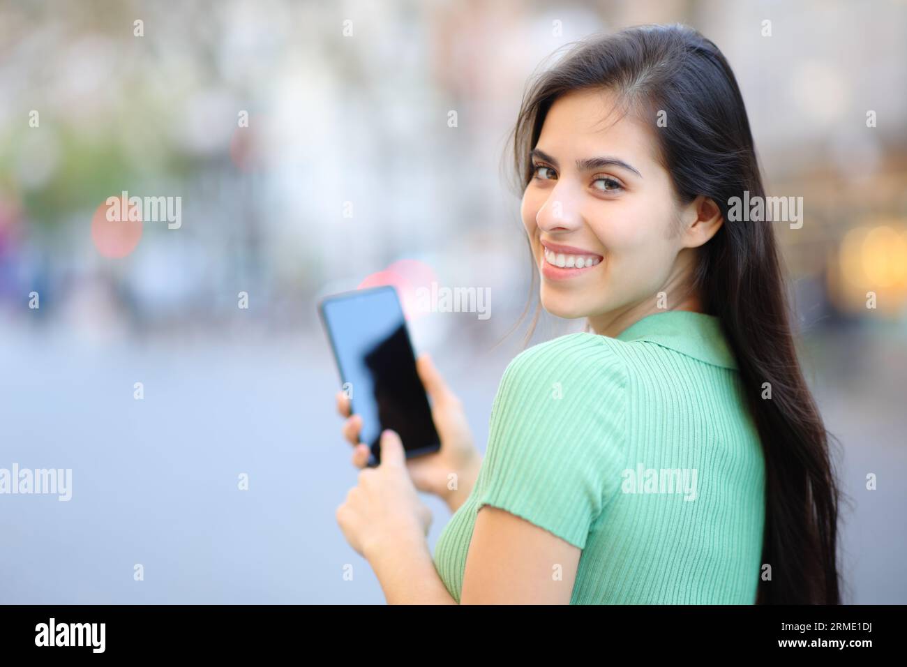 Glückliche Frau, die mit dem Handy herumwirbelt und auf der Straße auf die Kamera schaut Stockfoto