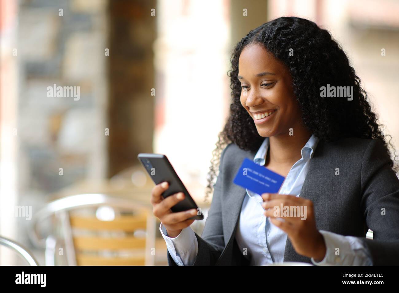 Glückliche schwarze Geschäftsfrau, die online mit Kreditkarte und Smartphone in einer Bar-Terrasse kauft Stockfoto