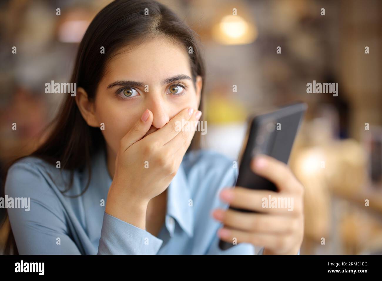 Eine schockierte Frau, die ein Smartphone in einer Bar hält, sieht dich an Stockfoto