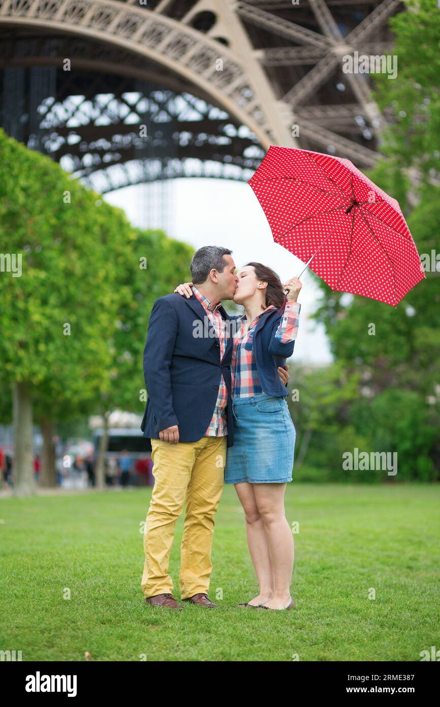 Ehepaar unter rotem Schirm in der Nähe des Eiffelturms Stockfoto