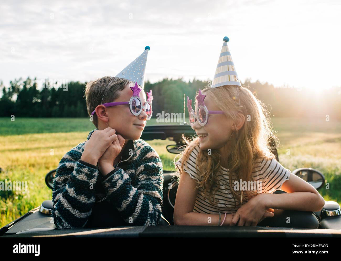 Mädchen und Jungen saßen in einem Cabriolet mit Partyhüten und Brille Stockfoto