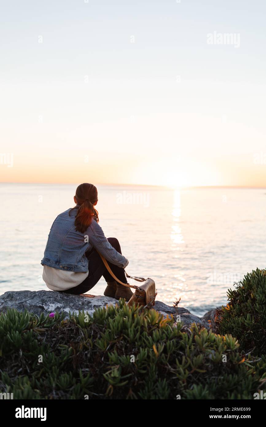 Eine Frau, die einen Sonnenuntergang an einer felsigen Küste beobachtet Stockfoto