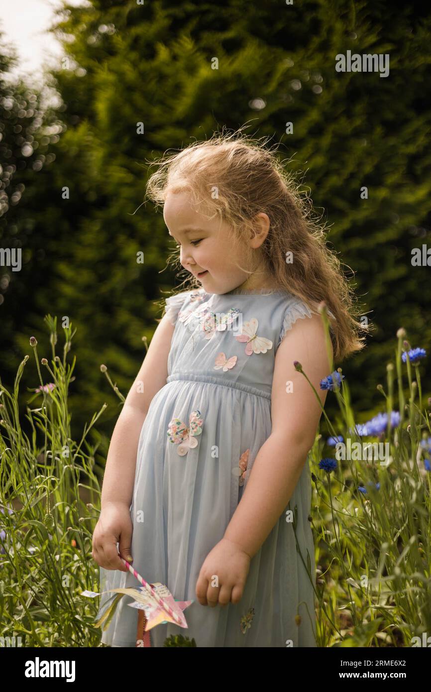 Das junge Mädchen im Schmetterlingskleid genießt den Wildblumengarten Stockfoto