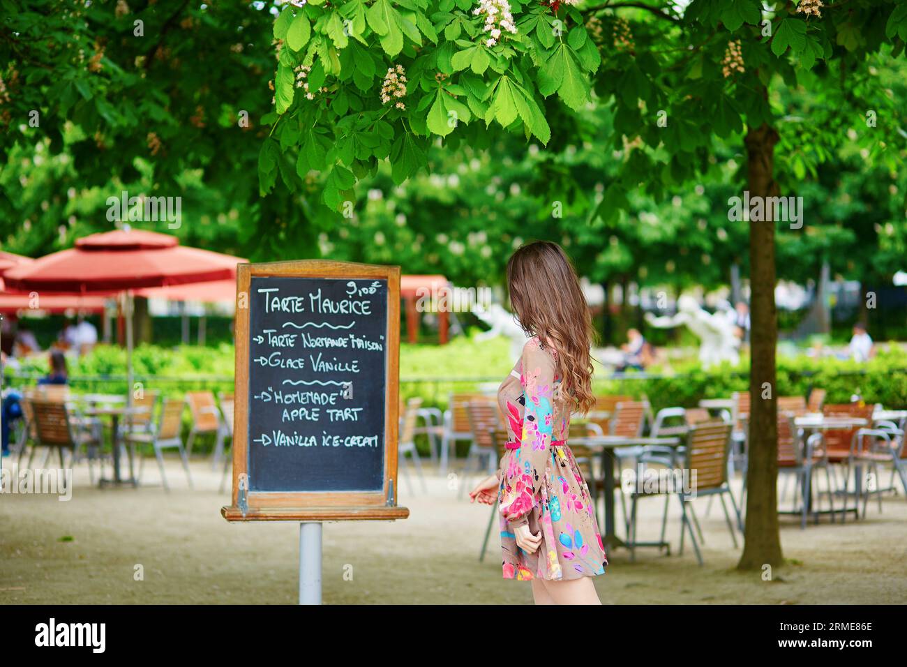 Schöne junge Pariser Frau, die an einem sonnigen Sommertag in einem Pariser Restaurant im Tuileriegarten ein handgeschriebenes Menü liest Stockfoto