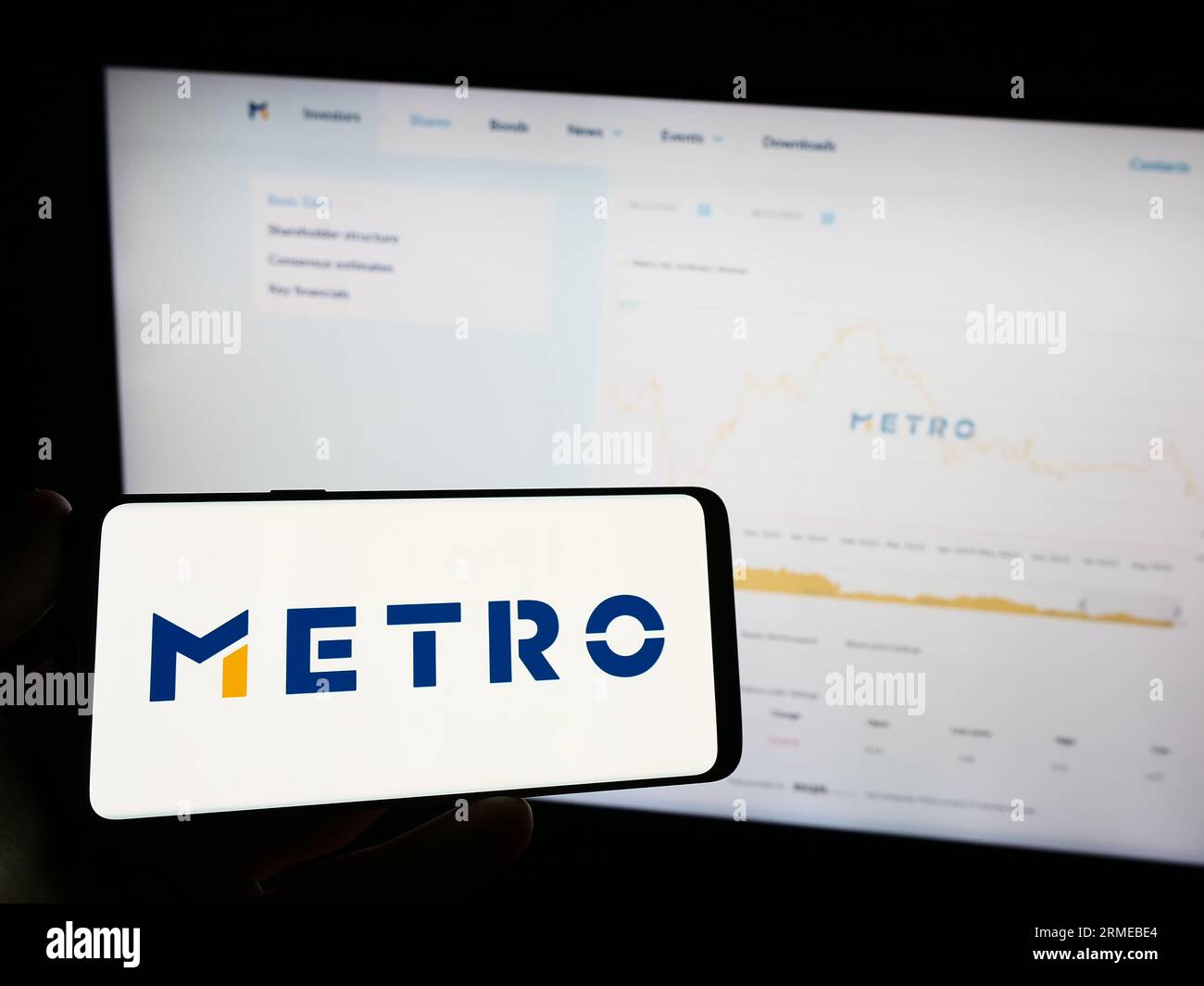 Person, die ein Mobiltelefon mit dem Logo des deutschen Großhandelsunternehmens Metro AG auf dem Bildschirm vor der Business-Webseite hält. Konzentrieren Sie sich auf das Display des Telefons. Stockfoto
