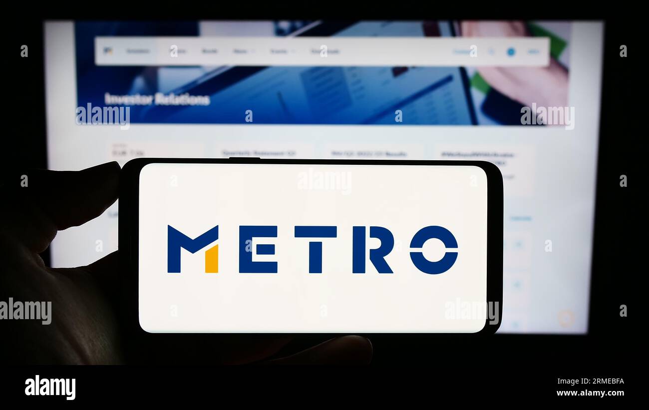 Person, die ein Mobiltelefon mit dem Logo des deutschen Großhandelsunternehmens Metro AG auf dem Bildschirm vor der Geschäftswebseite hält. Konzentrieren Sie sich auf das Display des Telefons. Stockfoto