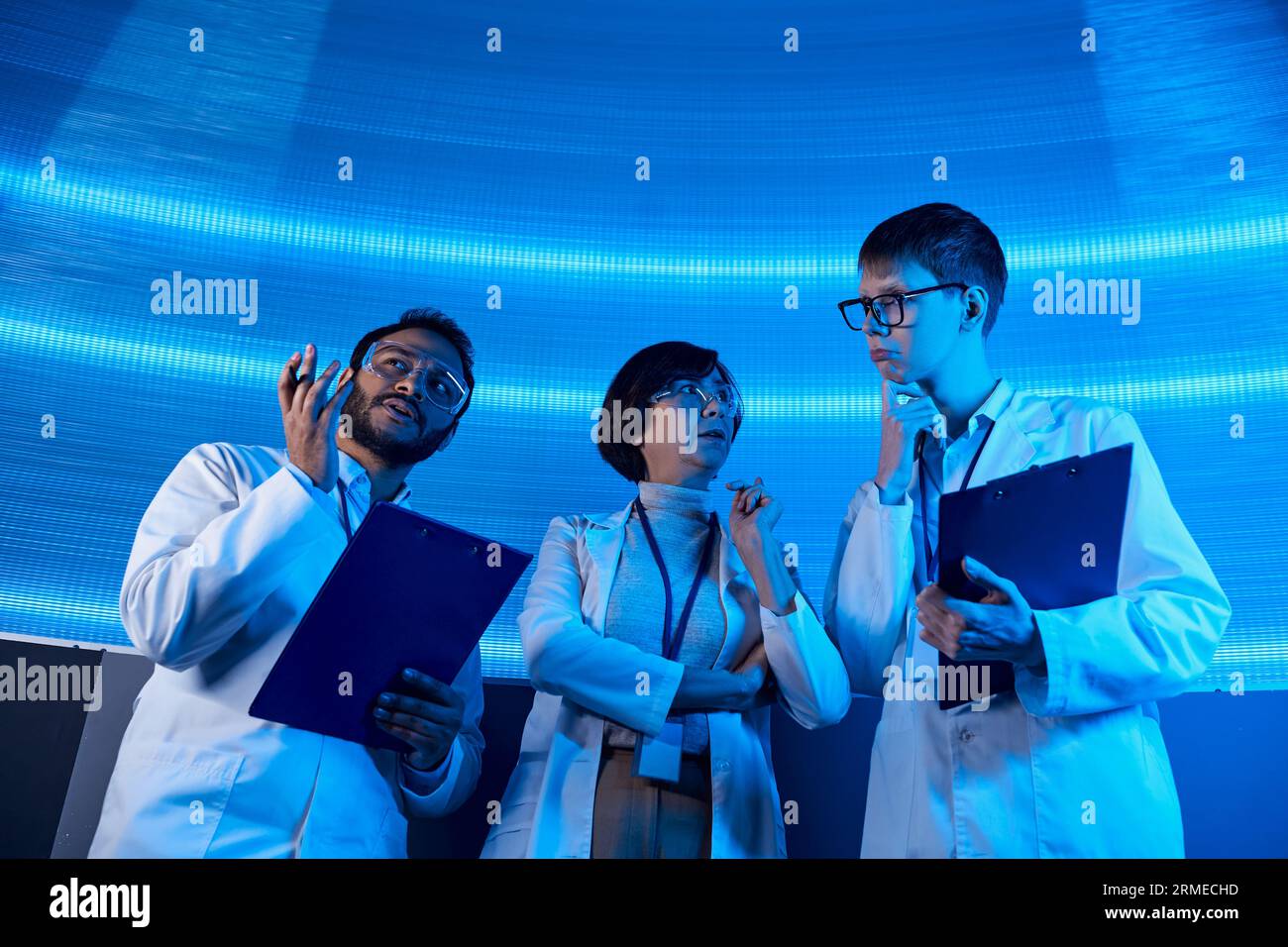 Futuristische Lösungen, multiethnische Wissenschaftler mit Klemmbrettern, die im neonbeleuchteten Discovery Center sprechen Stockfoto