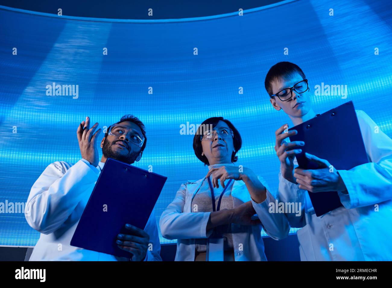 indischer Wissenschaftler zeigt mit Händen in der Nähe von Kollegen im Wissenschaftszentrum, zukunftsorientiert Stockfoto