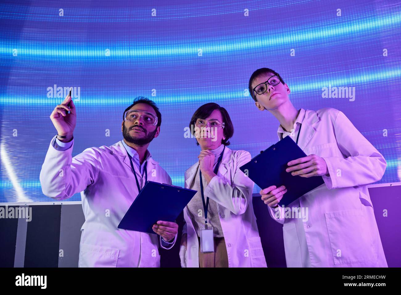 Zukunftsorientierter indischer Wissenschaftler zeigt mit Pen in der Nähe des Teams im innovativen Wissenschaftszentrum Stockfoto