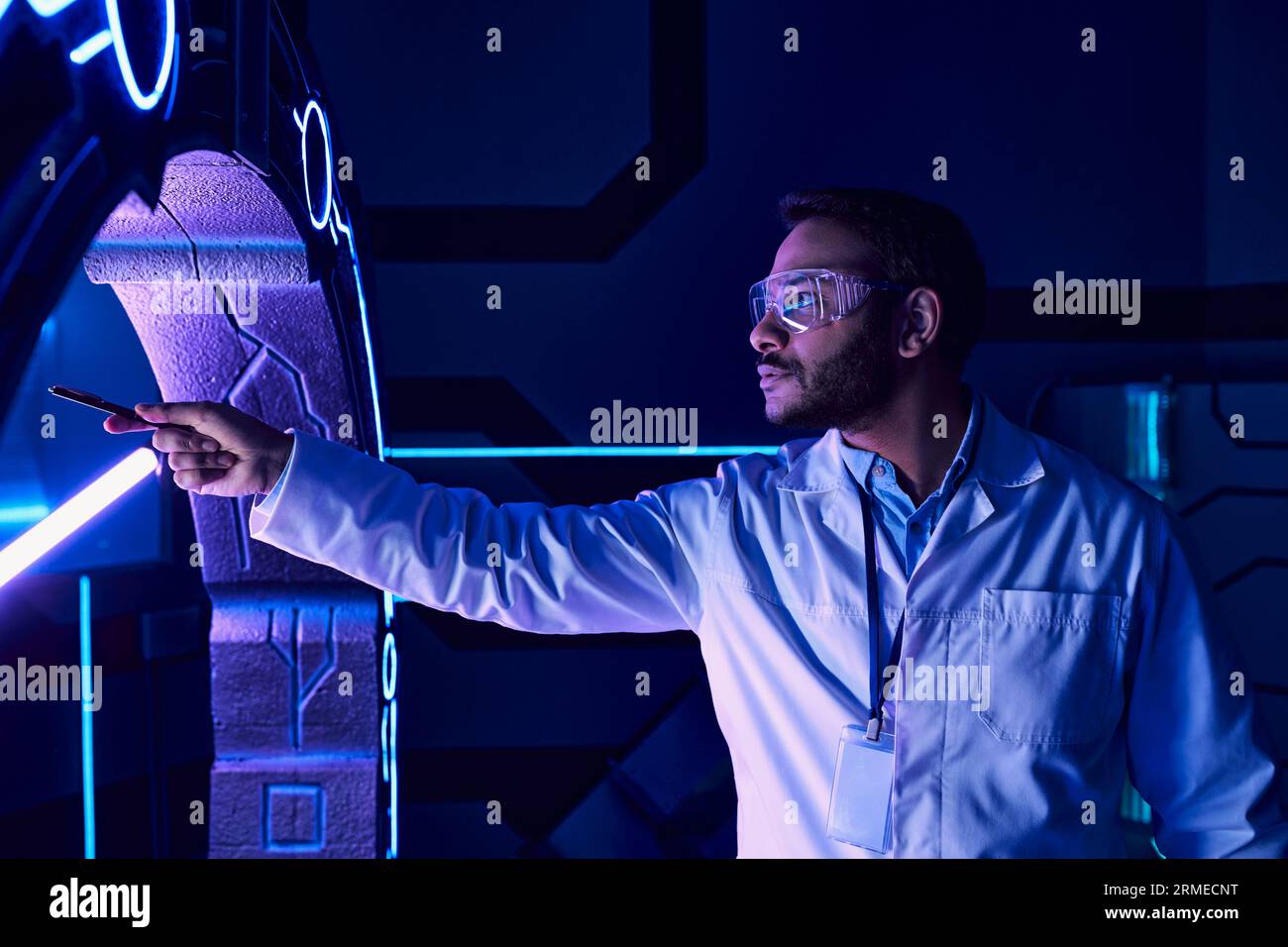 Futuristisches Konzept, indischer Brillenwissenschaftler, der mit Stift auf ein neues Gerät im Wissenschaftszentrum zeigt Stockfoto