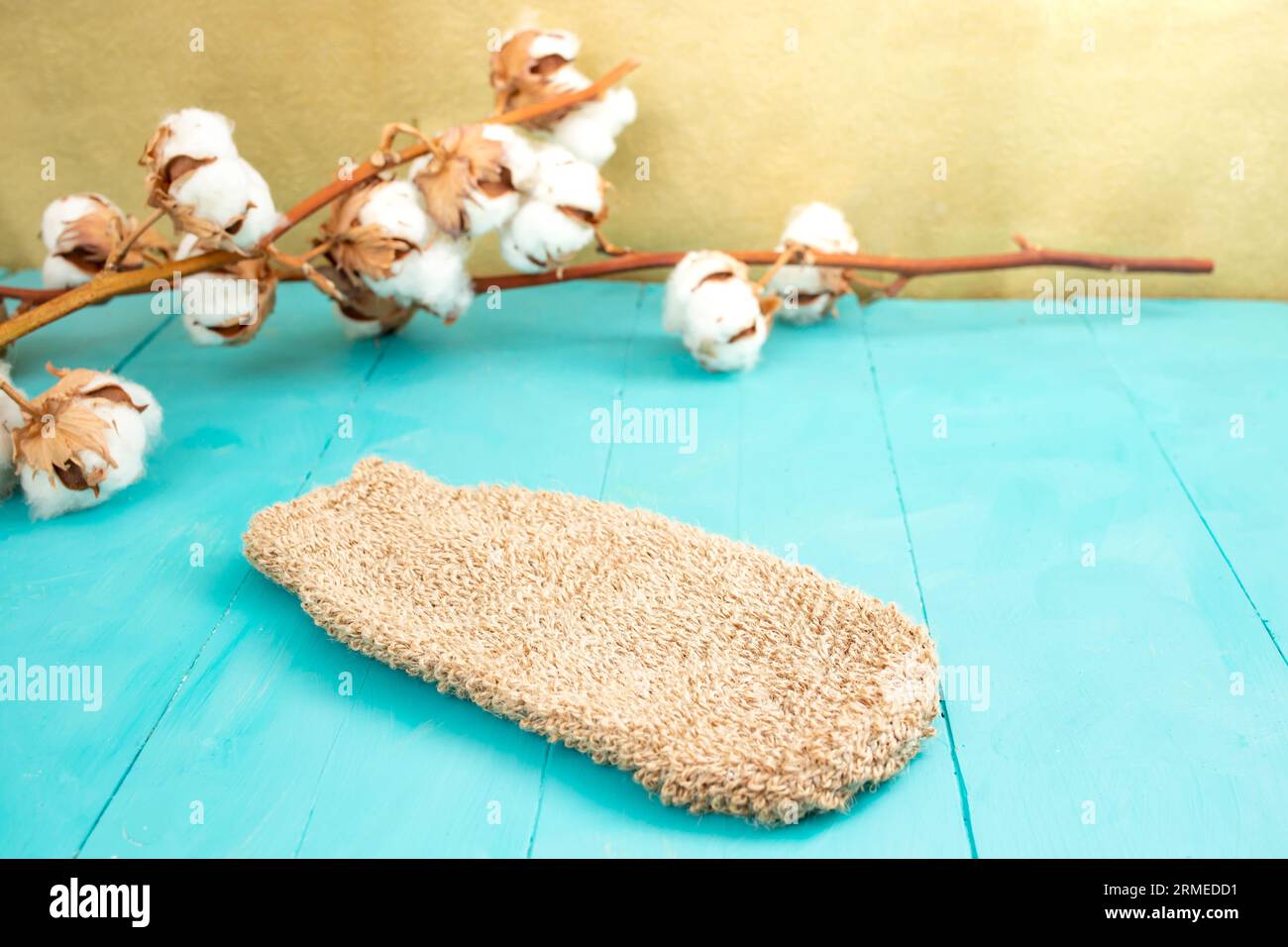 Badezimmerhintergrund mit einem Jutehandschuh und Blütenknospen aus Baumwolle auf blauen Holzbrettern und goldenem Hintergrund Stockfoto