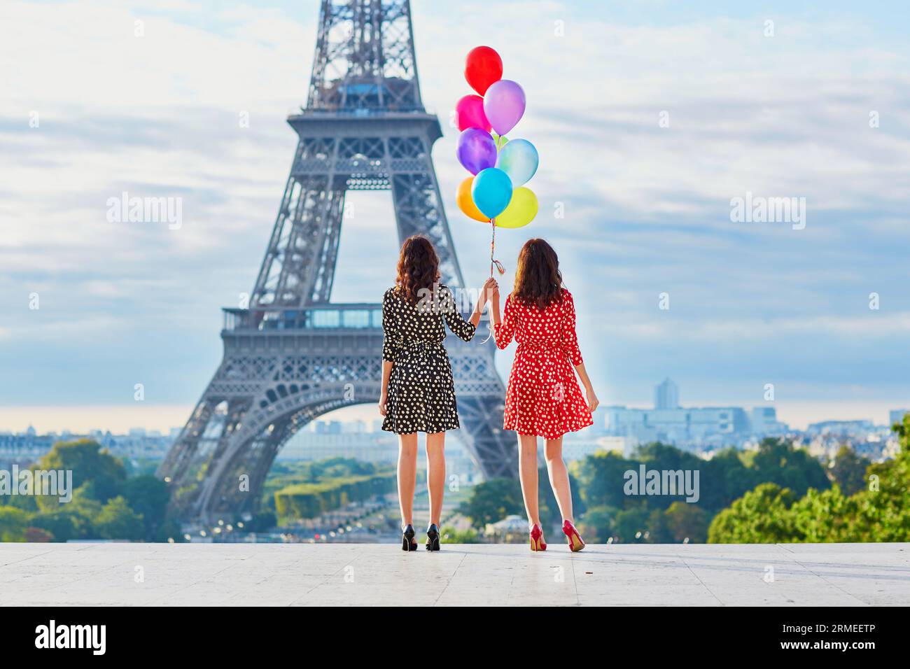 Wunderschöne Zwillingsschwestern in roten und schwarzen Polka-Dot-Kleidern mit riesigen bunten Ballons vor dem Eiffelturm in Paris, Frankreich Stockfoto