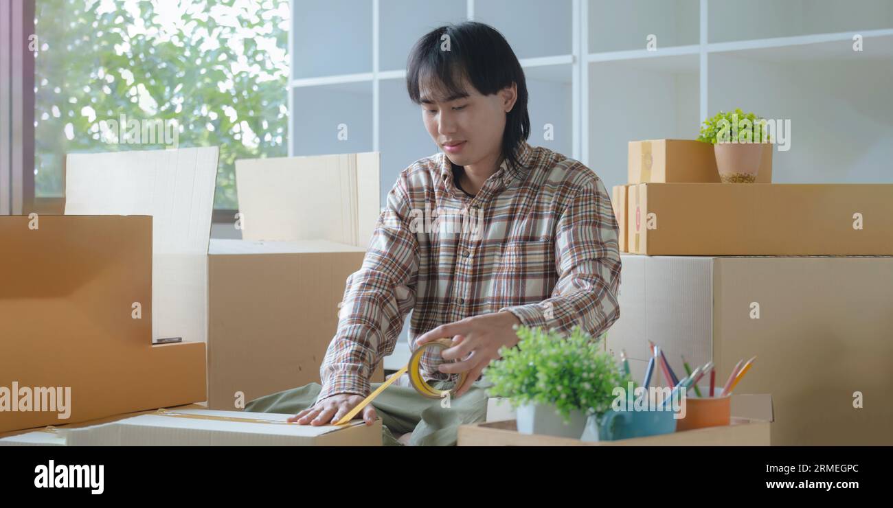 Young asian man smiling confident unpacking cardboard box at new home Stockfoto