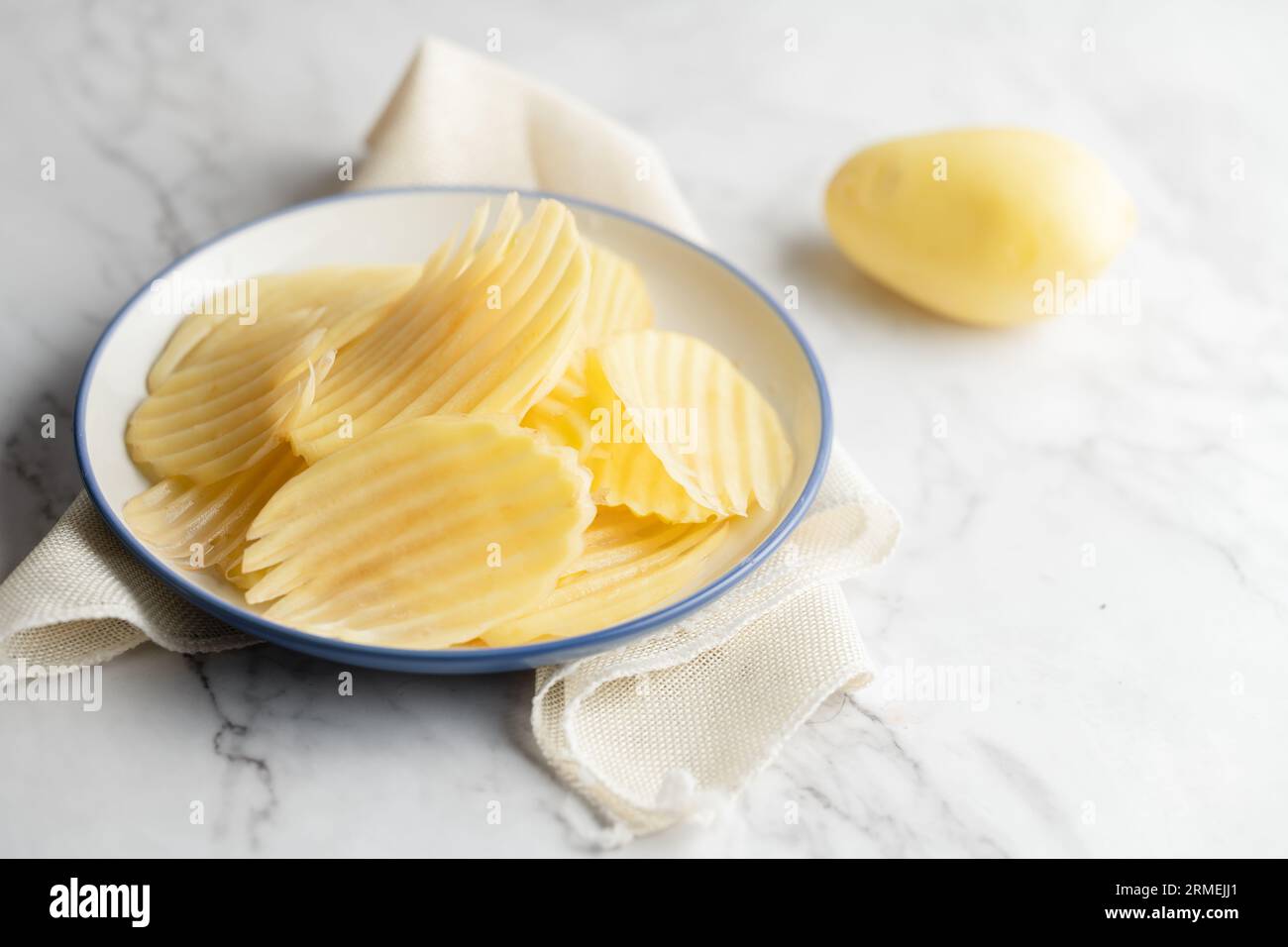 Scheiben und ganze Kartoffeln auf einem weißen Marmorbrett. Stockfoto