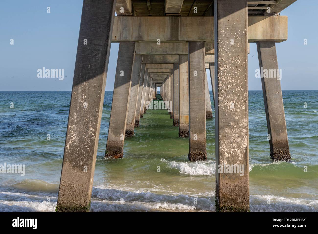 Ein ruhiger Pier, der auf das Meer hinausragt, mit Wellen, die auf das Ufer stürzen Stockfoto