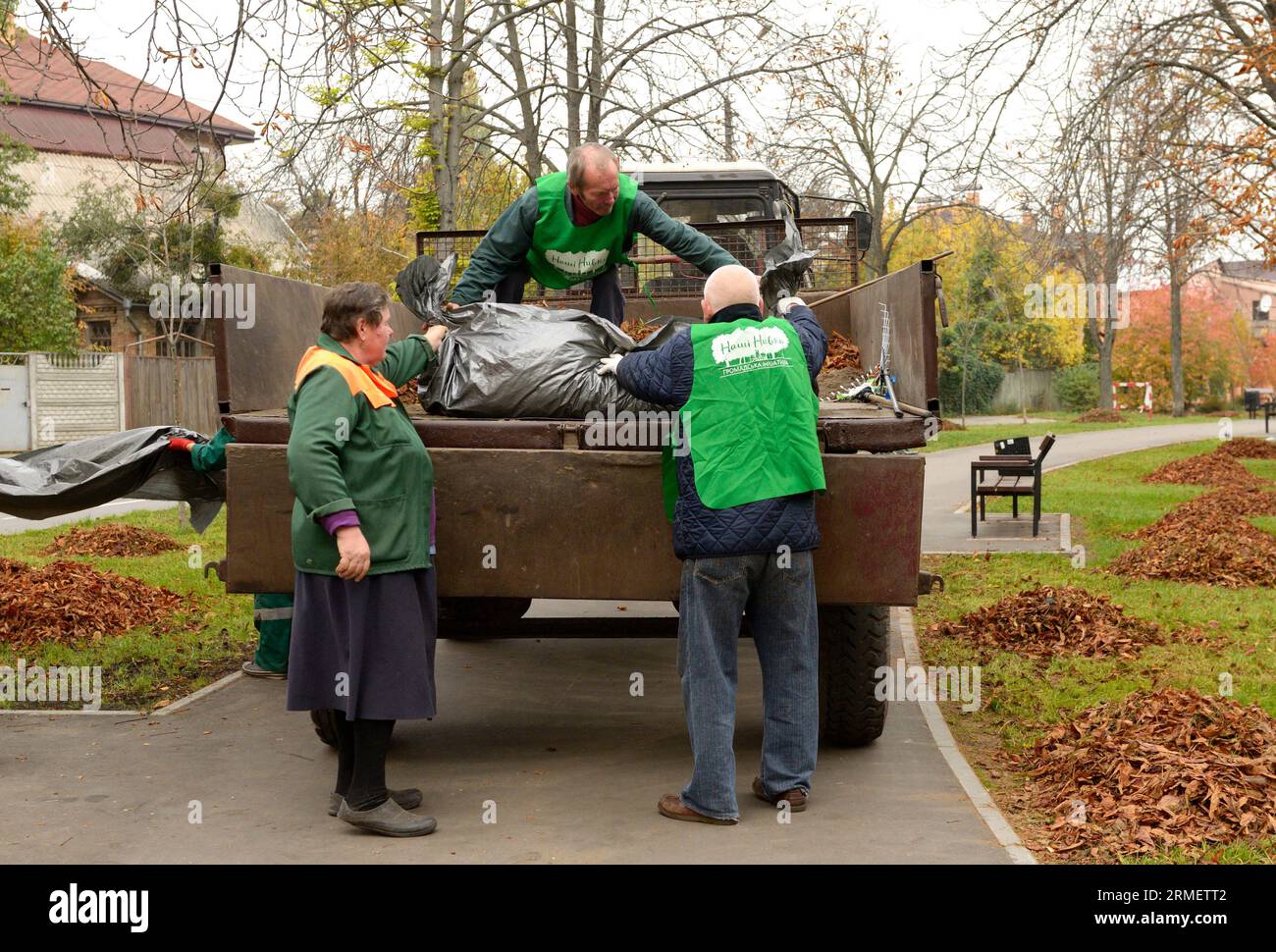 Reinigungsparks: Kommunale Kehrmaschinen, die Laubstapel auf einen Anhänger eines Traktors laden. Oktober 2017. Park Nivki. Kiew, Ukraine Stockfoto