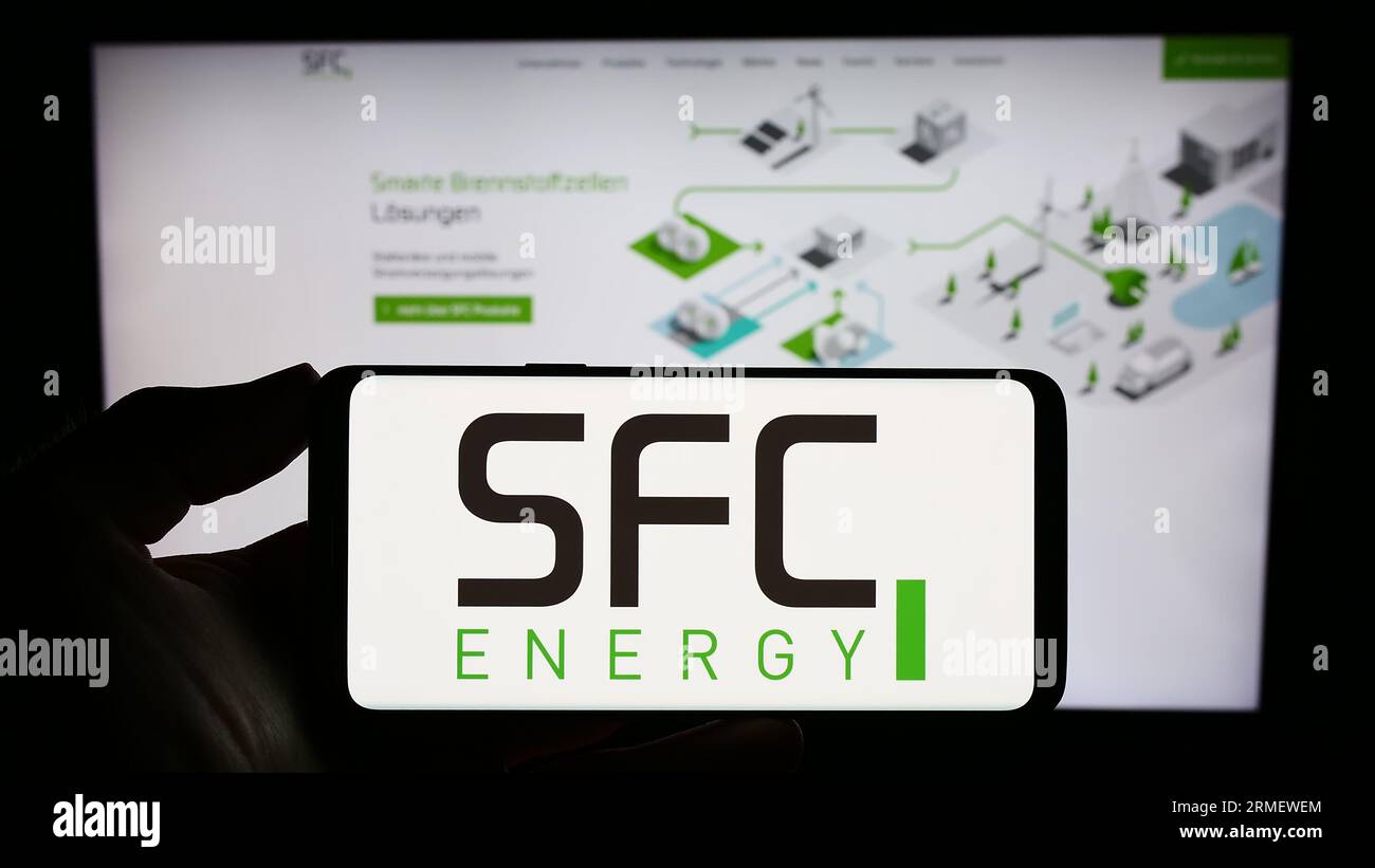 Person mit Smartphone mit Logo der SFC Energy AG auf dem Bildschirm vor der Website. Konzentrieren Sie sich auf das Display des Telefons. Stockfoto