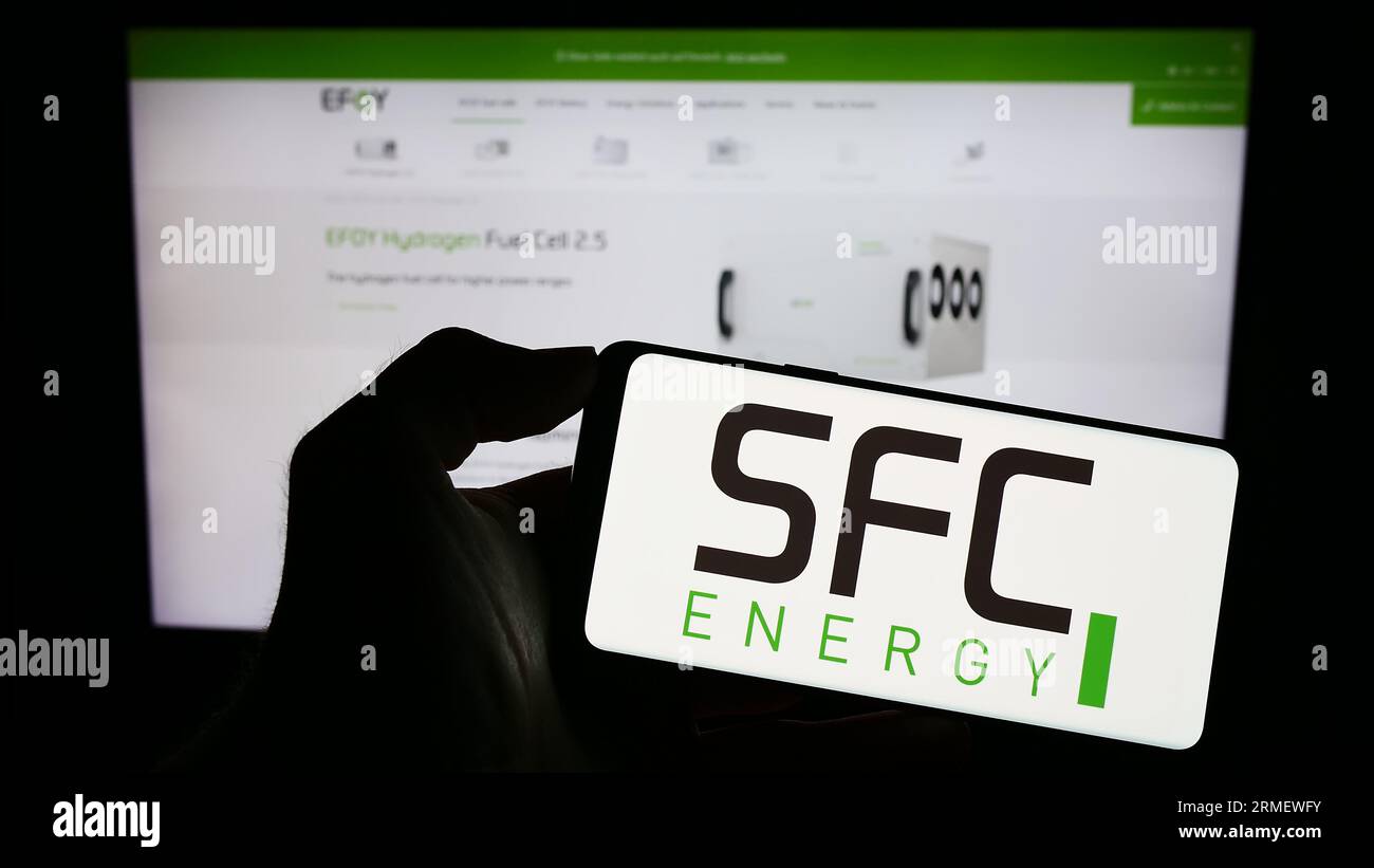 Person, die ein Mobiltelefon mit dem Logo der SFC Energy AG auf dem Bildschirm vor der Business-Webseite hält. Konzentrieren Sie sich auf das Display des Telefons. Stockfoto