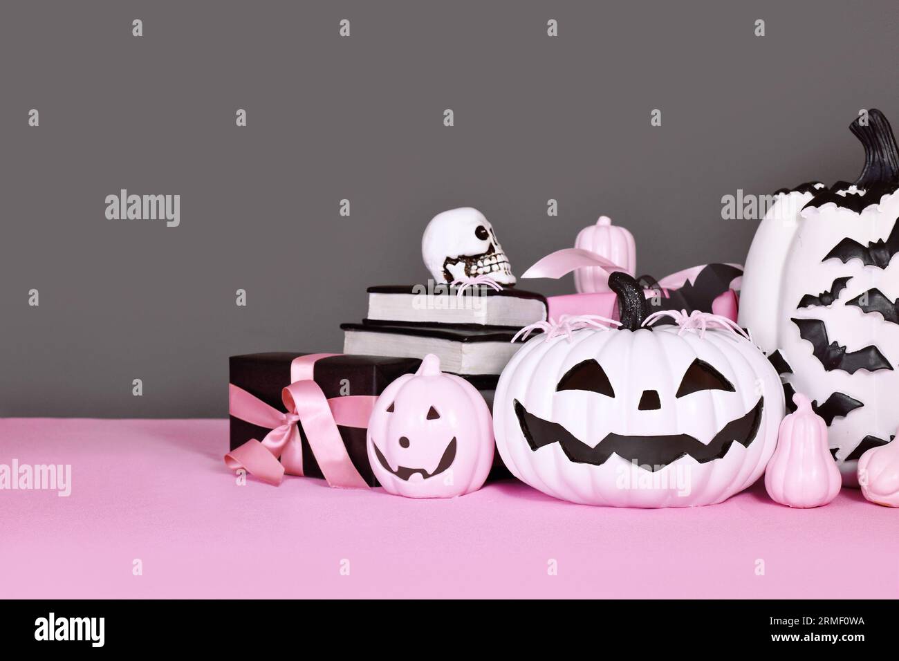 Rosafarbene und weiße Halloween-Einrichtung mit schwarz-weißen Kürbissen, Geschenkboxen und Zauberbüchern auf grauem Hintergrund Stockfoto