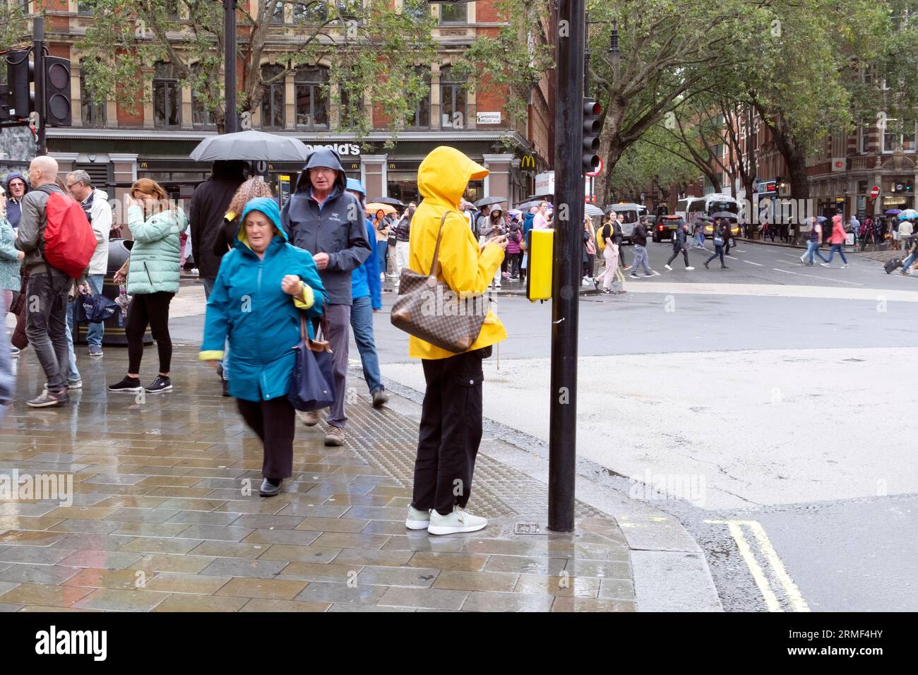 Menschen Fußgänger, die in der Straße gehen Frau trägt Regenmäntel Regenmantel an einem nassen regnerischen Sommertag August wartet an der Verkehrsampel London KATHY DEWITT Stockfoto