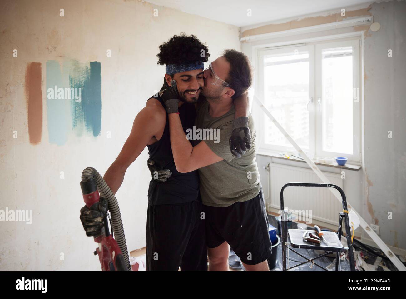 Männliches homosexuelles Paar küsst sich bei der Renovierung seiner Wohnung Stockfoto