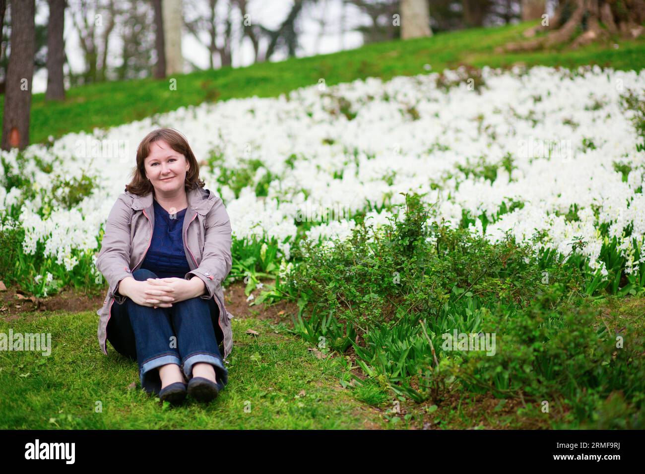 Hübsches junges Mädchen, das mit Hyazinthen auf dem Gras sitzt Stockfoto