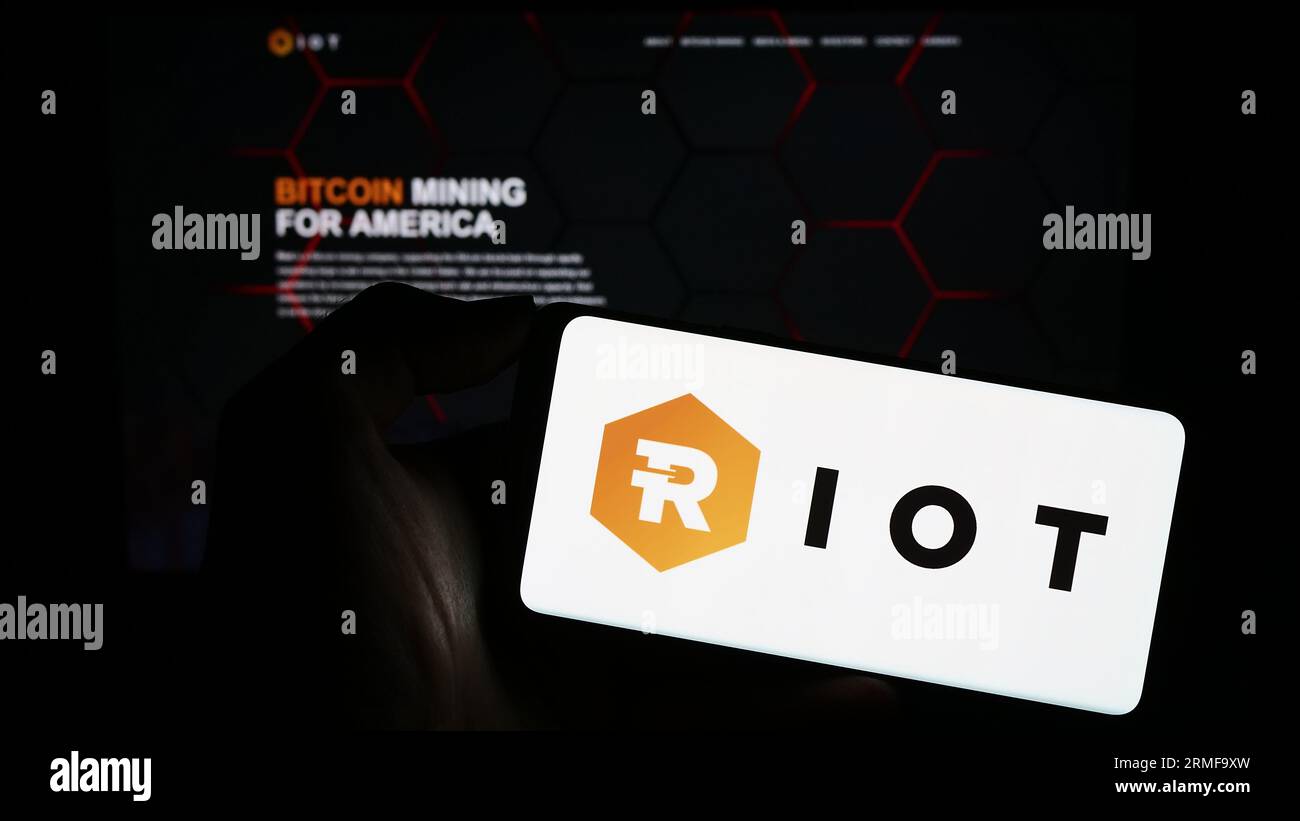 Person, die ein Mobiltelefon mit dem Logo des amerikanischen Bitcoin-Mining-Unternehmens Riot Platforms Inc. Auf dem Bildschirm vor der Webseite hält. Konzentrieren Sie sich auf das Display des Telefons. Stockfoto