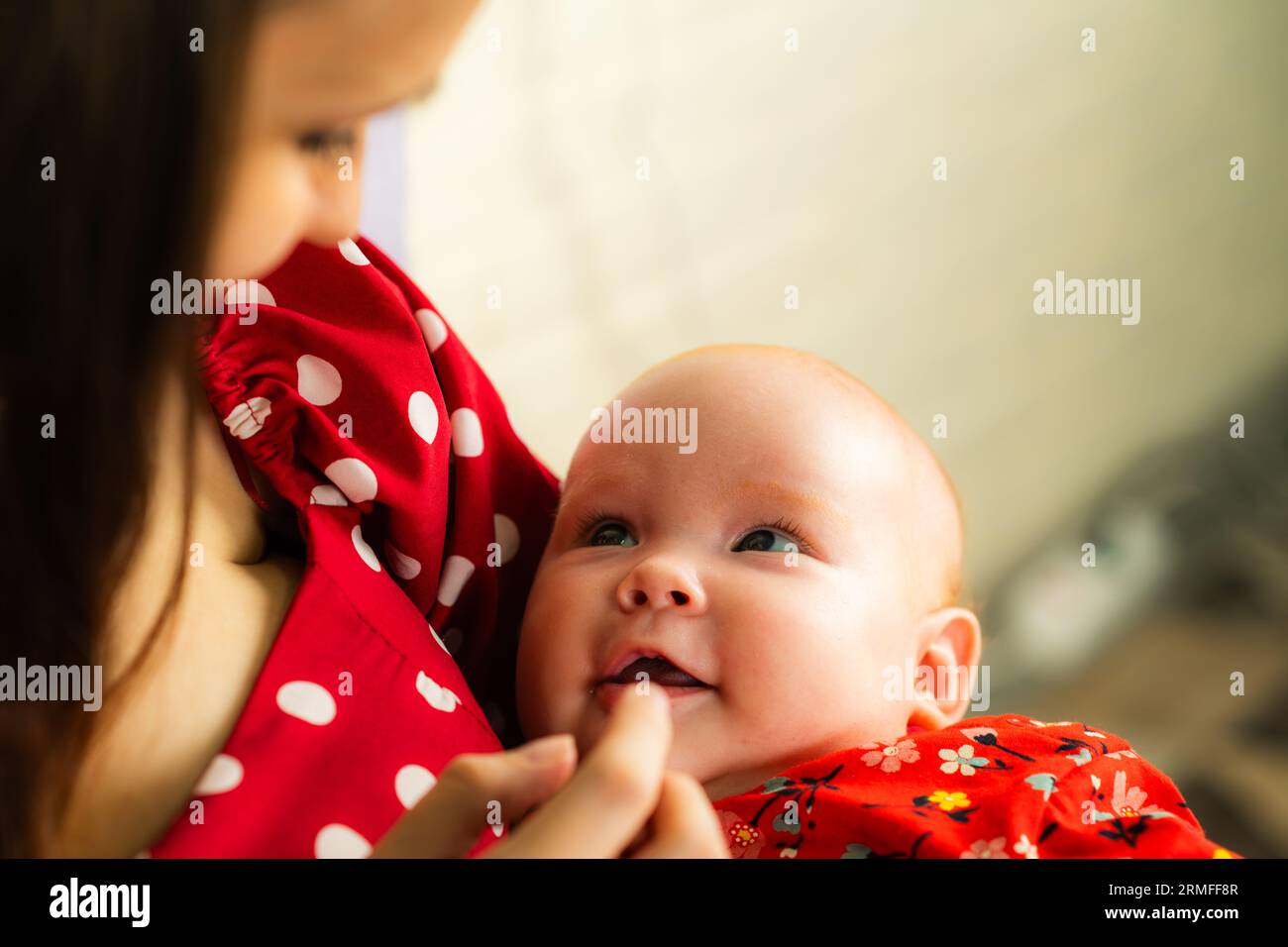 Neugeborenes Mädchen an den Händen der Mutter in rotem Polka-Dot-Kleid Stockfoto