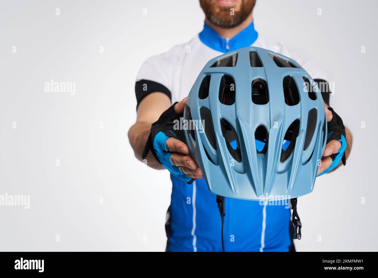 Nicht erkennbarer bärtiger Radfahrer, der modernen Helm vor der Kamera zeigt. Nahaufnahme des Schutzhelms, dargestellt von Mann im Fahrradkit, isoliert auf weiß Stockfoto