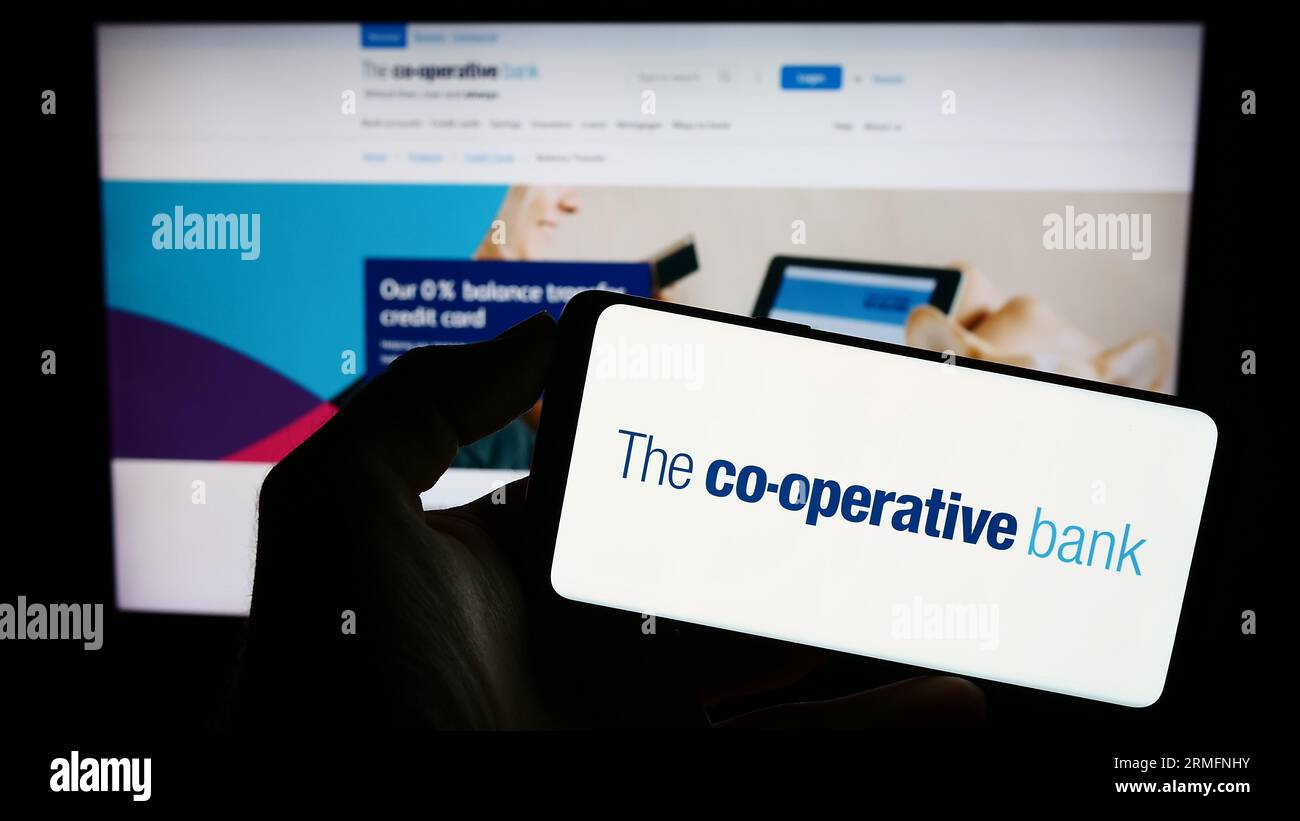 Person, die ein Mobiltelefon mit dem Logo des britischen Unternehmens The Co-operative Bank plc auf dem Bildschirm vor der Webseite hält. Konzentrieren Sie sich auf das Display des Telefons. Stockfoto