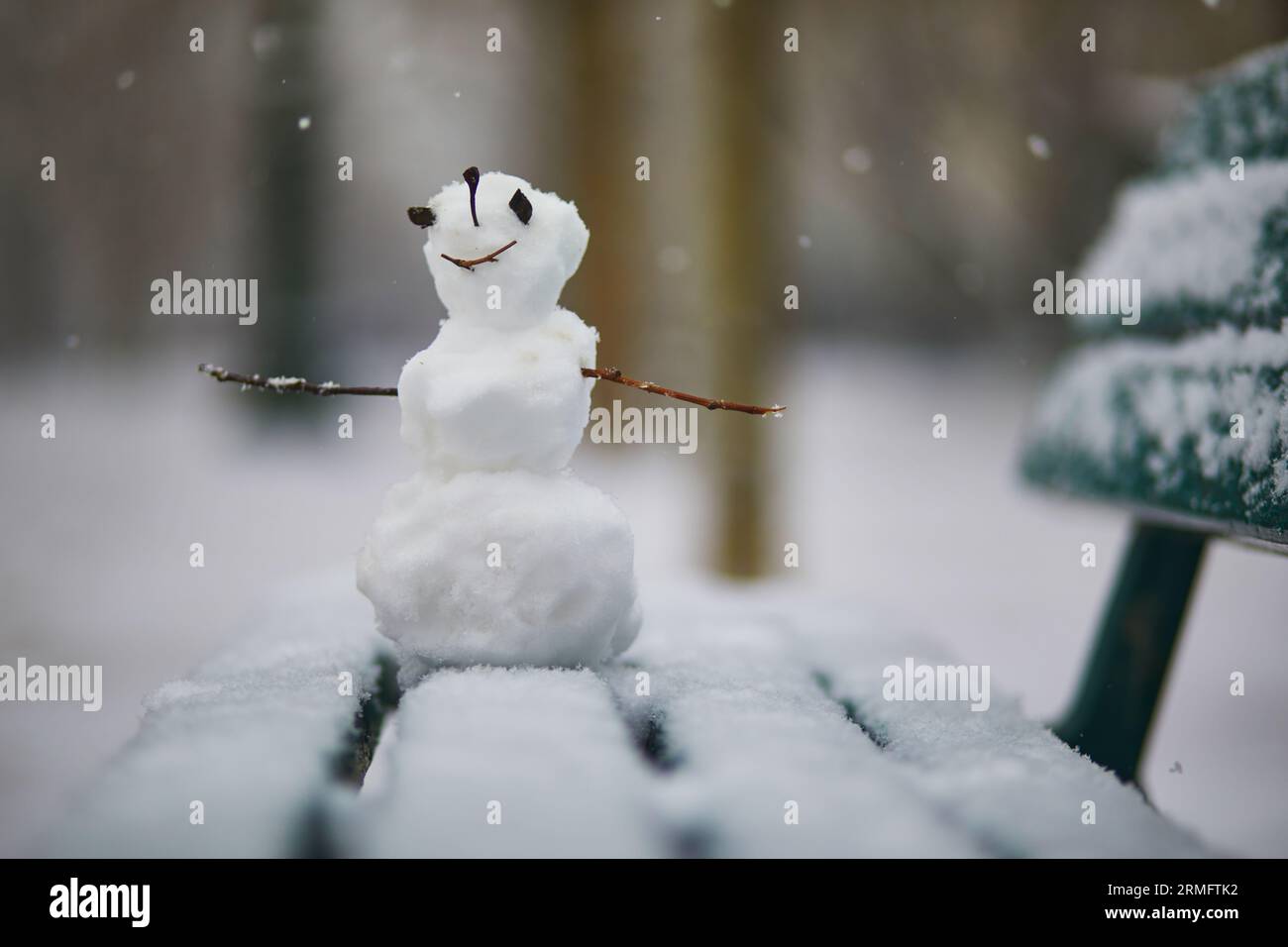 Kleiner Schneemann mit glücklichem Gesicht auf einer mit Schnee bedeckten Bank. Winteraktivitäten mit Kindern. Kaltes, schneebedecktes Wetter Stockfoto