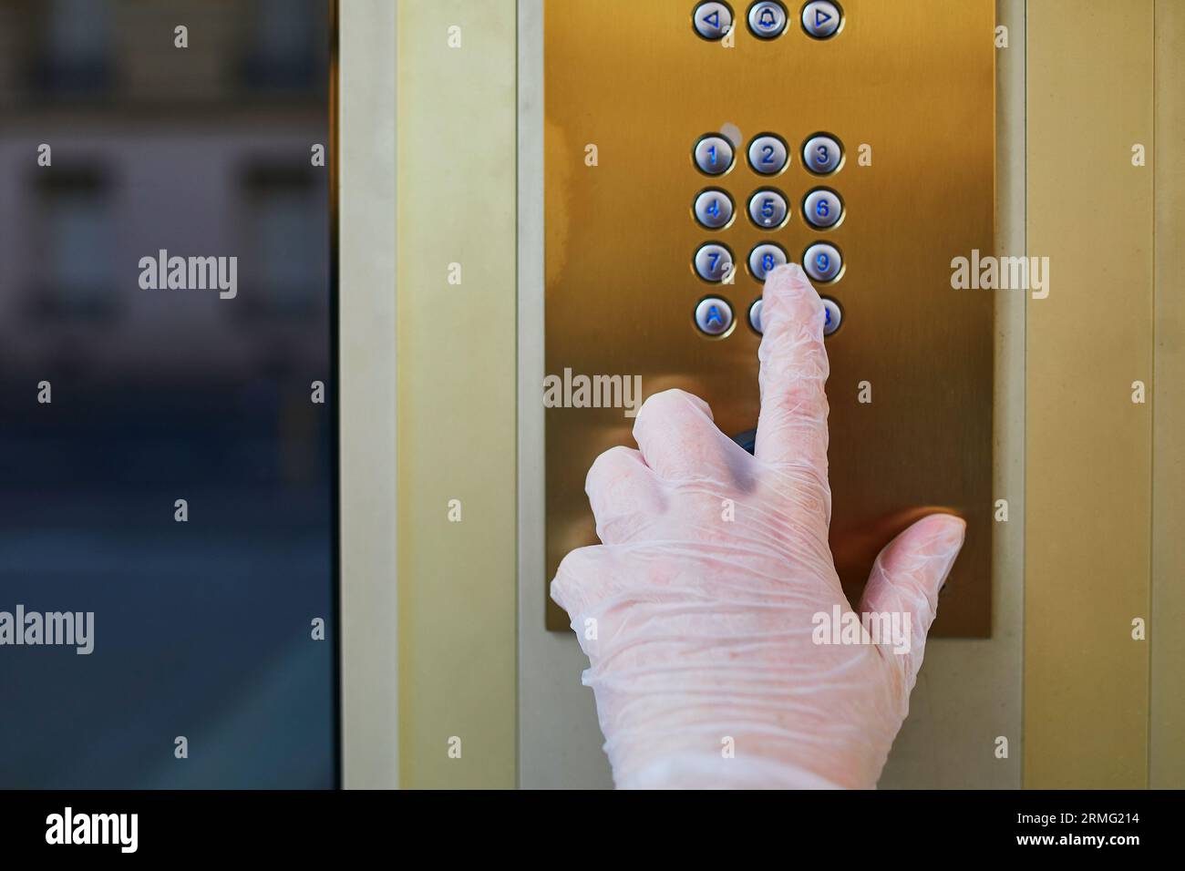 Frau Hand in schützenden Einweghandschuh drückt Haus Intercome Knopf in einem Wohnhaus Gebäude. Quarantäne und Selbstisolierung während des PAN Stockfoto