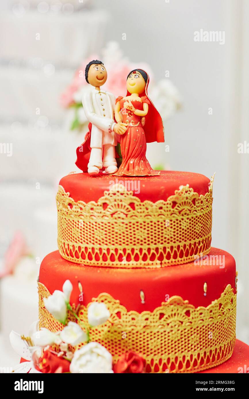 Wunderschöne rot-gelbe Hochzeitstorte im indischen Stil mit Braut- und Bräutigam-Figuren auf der Oberseite Stockfoto