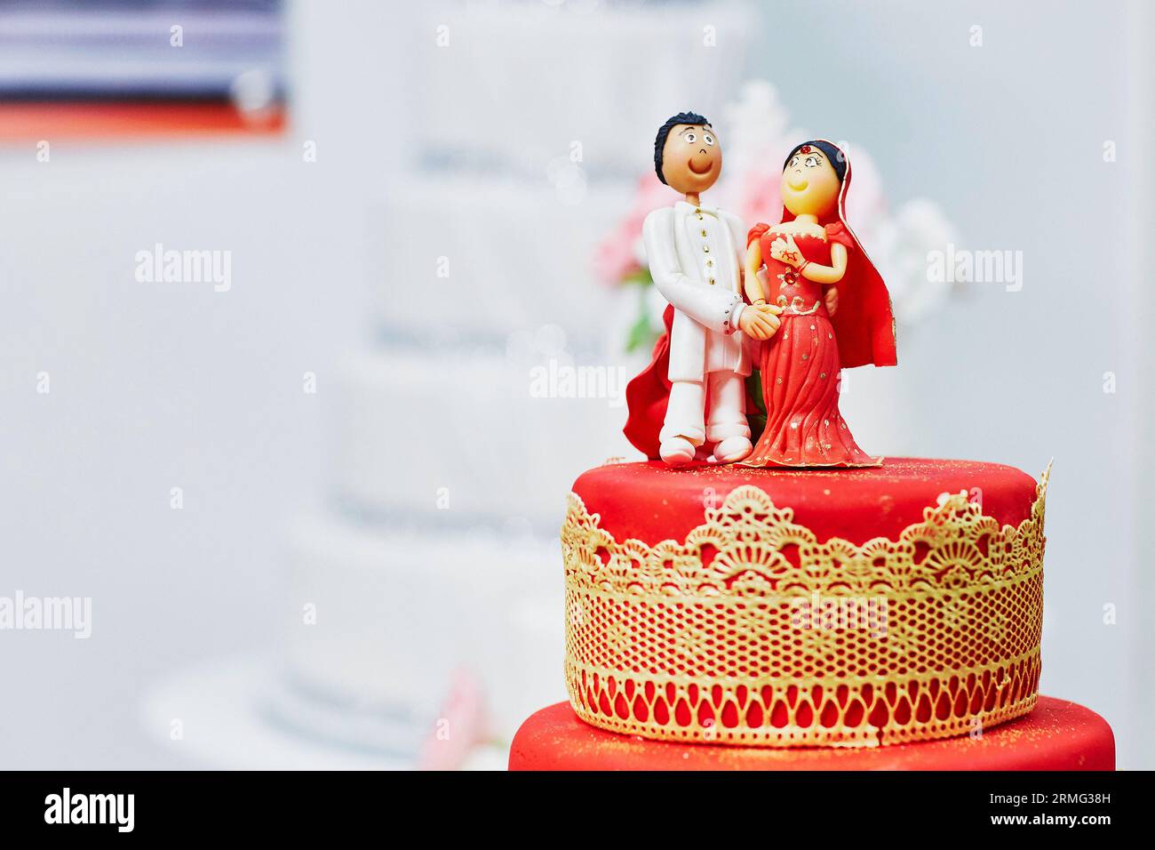 Wunderschöne rot-gelbe Hochzeitstorte im indischen Stil mit Braut- und Bräutigam-Figuren auf der Oberseite Stockfoto