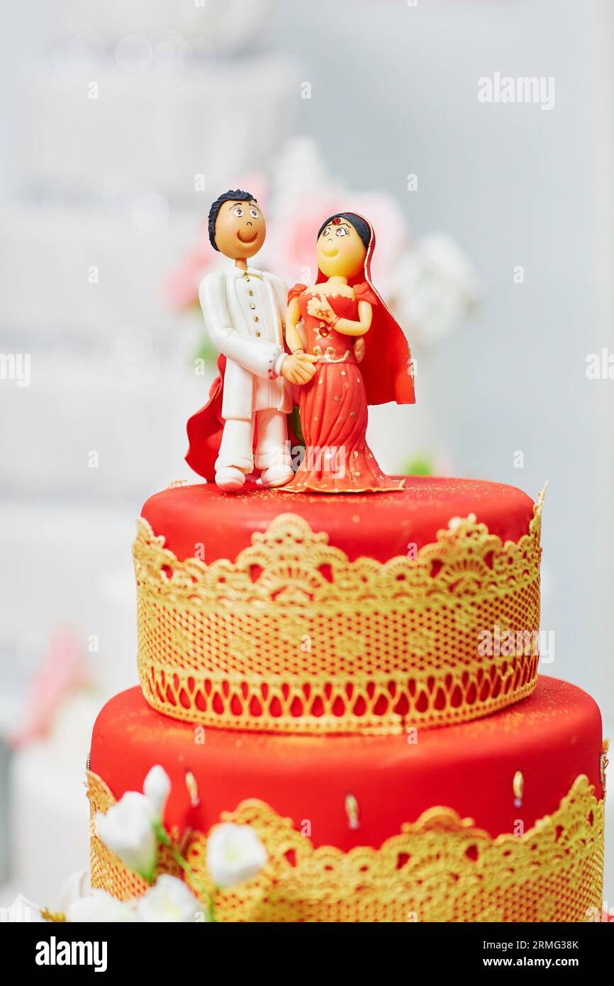 Wunderschöne rot-gelbe Hochzeitstorte im indischen Stil mit Braut- und Bräutigam-Figuren auf der Oberseite Stockfoto