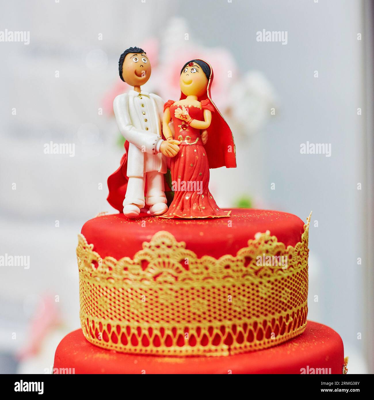 Wunderschöne rot-gelbe Hochzeitstorte im indischen Stil mit Braut- und Bräutigam-Figuren auf der Oberseite Stockfoto