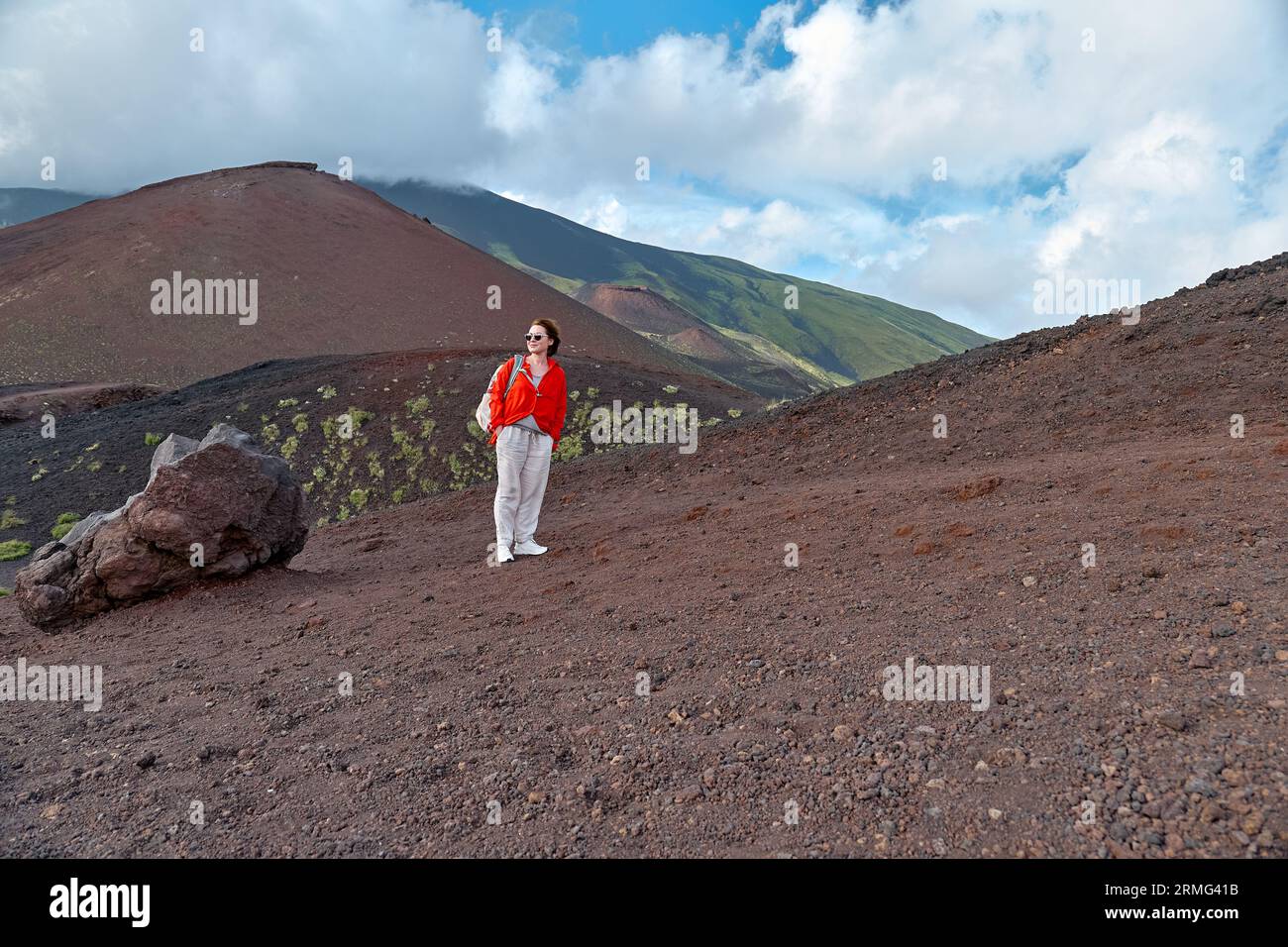 Wandern auf dem höchsten Vulkan Kontinentaleuropas - Ätna. Lächelnde junge Frau, die die Luft am Hang genießt, bedeckt grüne Vegetation auf schwarzem Sand, Lavafelsen Stockfoto