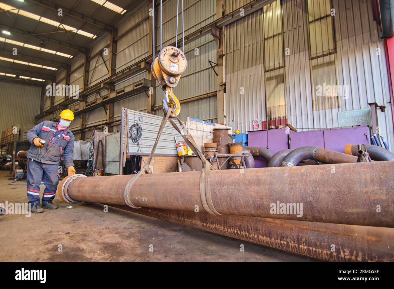 Männer, die einen Aufzug und einen Kran verwenden, um große, schwere Metallgegenstände wie Pips in einer Werkstatt/Fabrik zu bewegen. Menschen bewegen Dinge Stockfoto