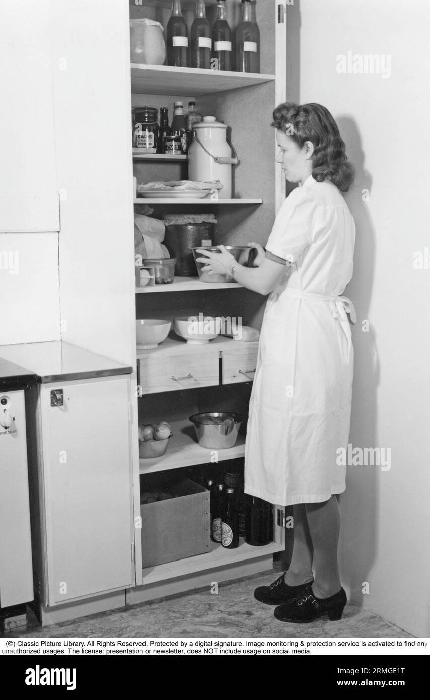 1940er Jahre Lagerung von Lebensmitteln. Eine Frau in der Küche und ein Schrank mit Regalen mit Lebensmittelzutaten und Lebensmitteln, die besser etwas kälter gehalten werden als die Zimmertemperatur. Gemüse, Marmelade und Limonade und mehr. Schweden 1948 Stockfoto
