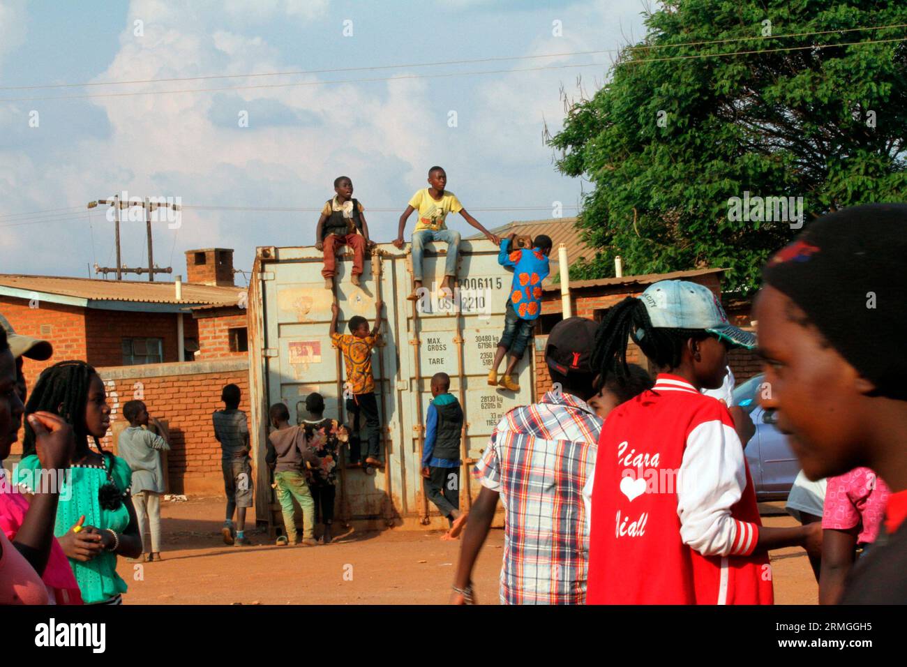 Junge Menschen sitzen auf einem Container, während andere versuchen, die Aktivitäten während eines Festivals im Dzaleka Refugee Camp im Bezirk Dowa in Malawi zu sehen. Stockfoto