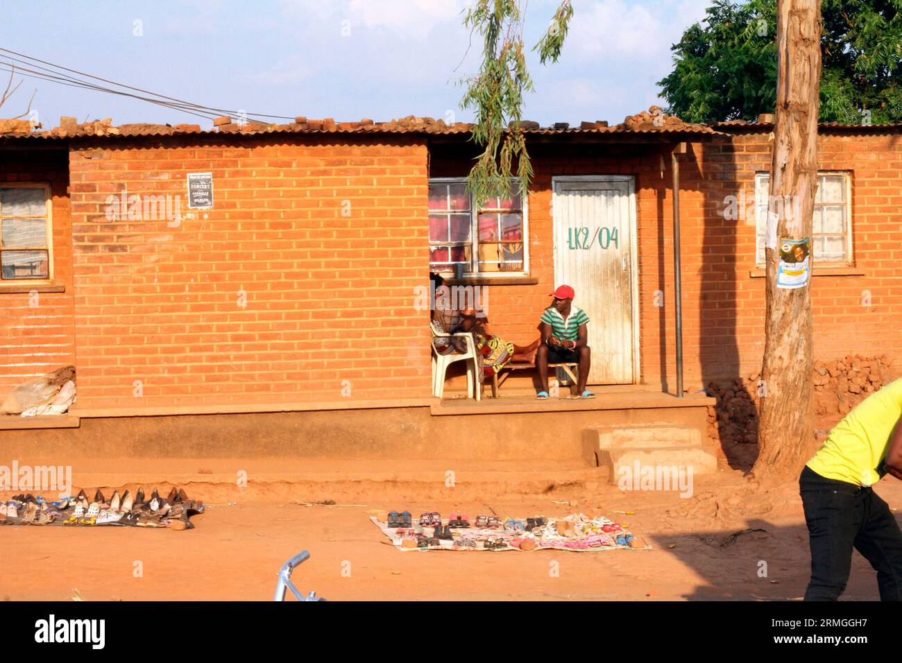 Eine Frau und ein Mann sitzen vor ihrem Haus, wo sie einen Markt auf dem Hof des Dzaleka Flüchtlingslagers im Bezirk Dowa, Malawi, eingerichtet hat. Stockfoto