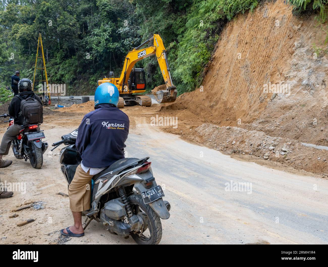 Männer auf dem Motorrad, die auf die Straßenbesatzung warten, die eine Bergstraße mit einem Bagger aufräumt. Sumatra, Indonesien. Stockfoto