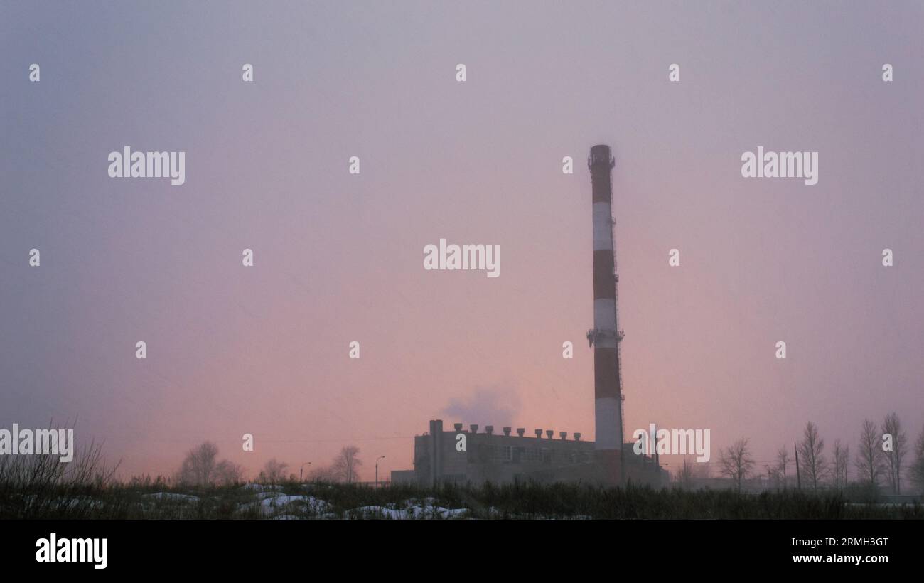 Der Kamin und das Gebäude des Kesselhauses im Nebel während eines Sturms vor dem Hintergrund des Lichts der Gewächshäuser Stockfoto